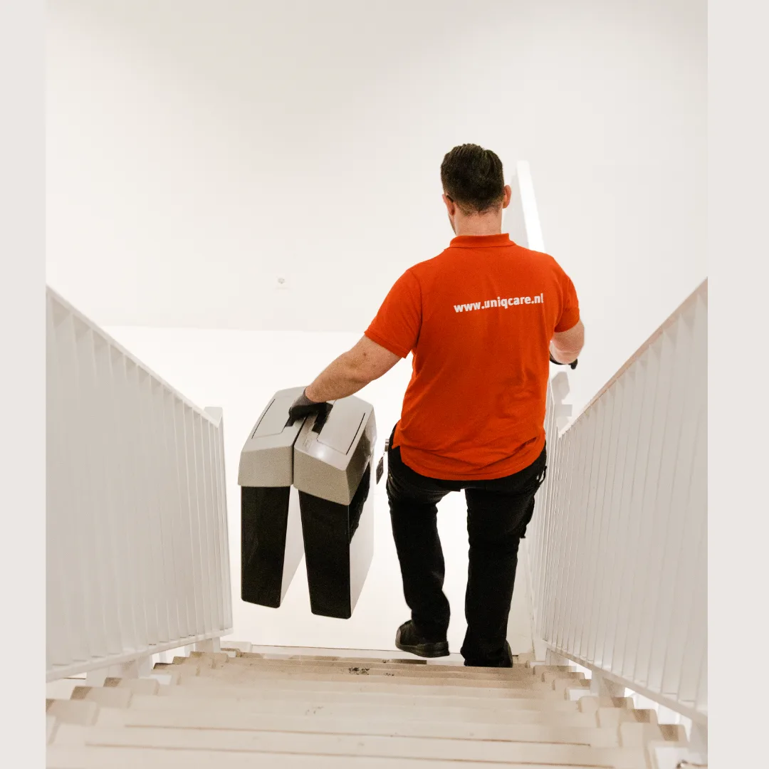 Een medewerker van Uniqcare draagt een hygiënebak de trap op